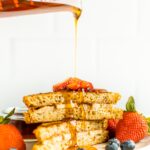 Pyrex measuring cup pouring maple syrup over two slices of stuffed french toast on a plate with berries.