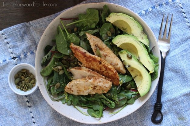 Power Greens Salad + Citrus Dressing by Fierce Forward Power Greens Salad + Citrus Dressing in white shallow bowl with pumpkin seeds and a fork on the side.