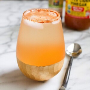 Apple pie drink in clear shallow glass sitting on a marble countertop with a silver spoon next to it.