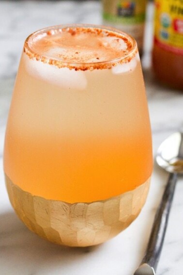 Apple pie drink in clear shallow glass sitting on a marble countertop with a silver spoon next to it.