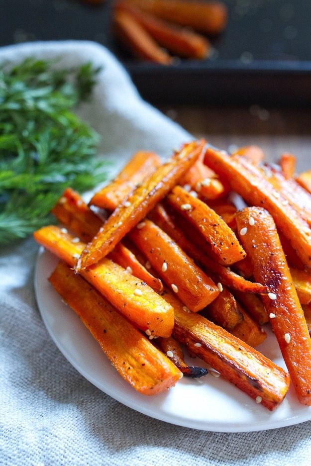 Sesame Roasted Carrots -- Easy enough for a weeknight meal, but fancy enough to serve to guests, these sesame roasted carrots are the perfect side dish. Vegan, gluten-free and lovely served hot or cold. White plate with sesame roasted carrots piled atop it.