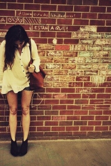 Brittany standing in front of a brick wall looking down at her shoes.