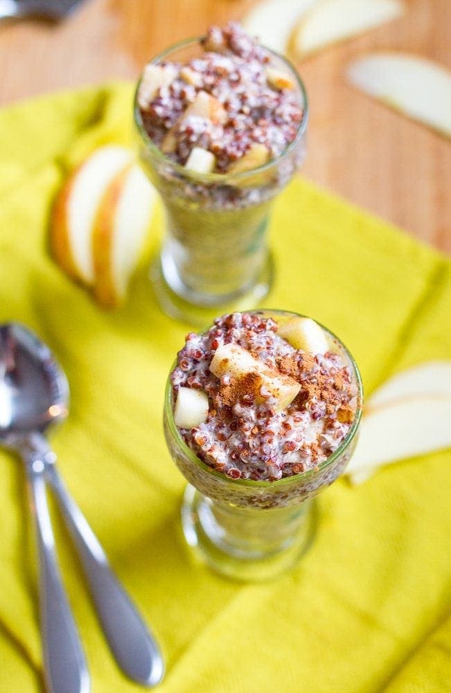 Apple Cinnamon Overnight Quinoa -- Turn leftover quinoa into a protein-packed breakfast with this simple, seasonal apple cinnamon overnight quinoa recipe that's gluten-free and vegan. Two tall, narrow glass jars with apple cinnamon overnight quinoa. There are two spoons and some apple slices on the table.