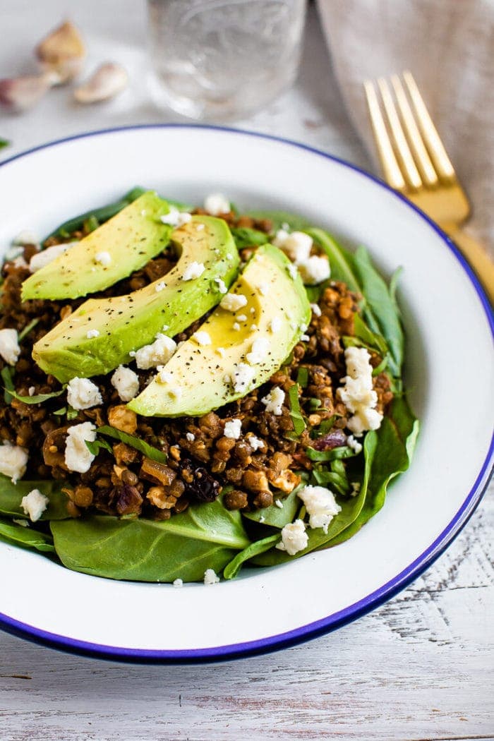 Plate with a bed of fresh spinach topped with a warm Mediterranean salad, topped with feta and avocado.