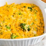 A broccoli quinoa casserole with cheddar cheese in a square white baking dish.