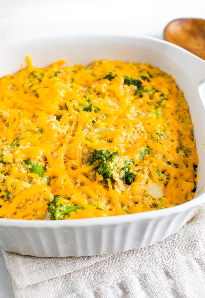 A broccoli quinoa casserole with cheddar cheese in a square white baking dish.