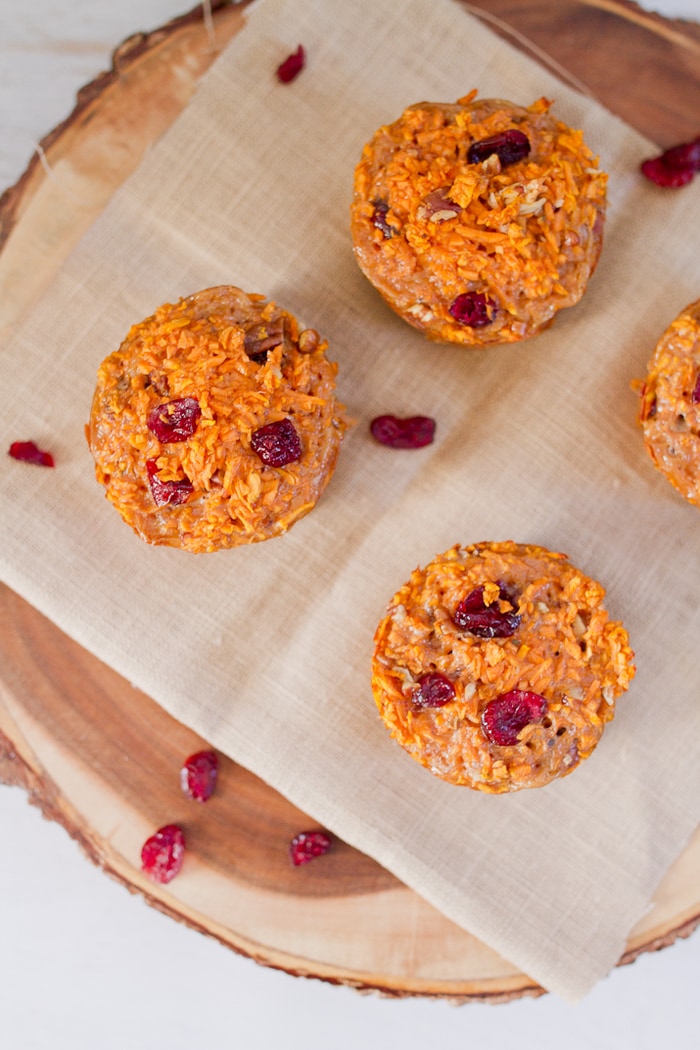 Spiralized cranberry pecan sweet potato muffins made with riced sweet potato noodles. They’re moist, filling and delicious served warm straight from the oven or at room temperature. Overhead photo of 4 muffins with cranberries sprinkled around.