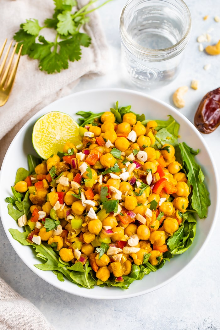 A bowl of curried chickpea salad made with chopped red onion, red pepper, cilantro, and dates, served over a bed of greens.