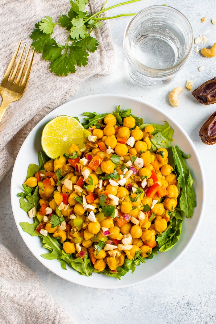 A serving of curried chickpea salad made with chopped red onion, red pepper, cilantro, and dates, served over a bed of greens.