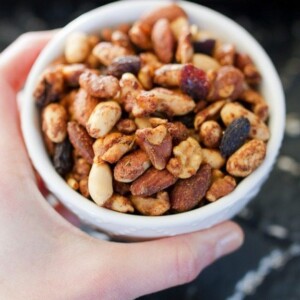 A woman's hand holding a small white bowl filled with cajun trail mix.