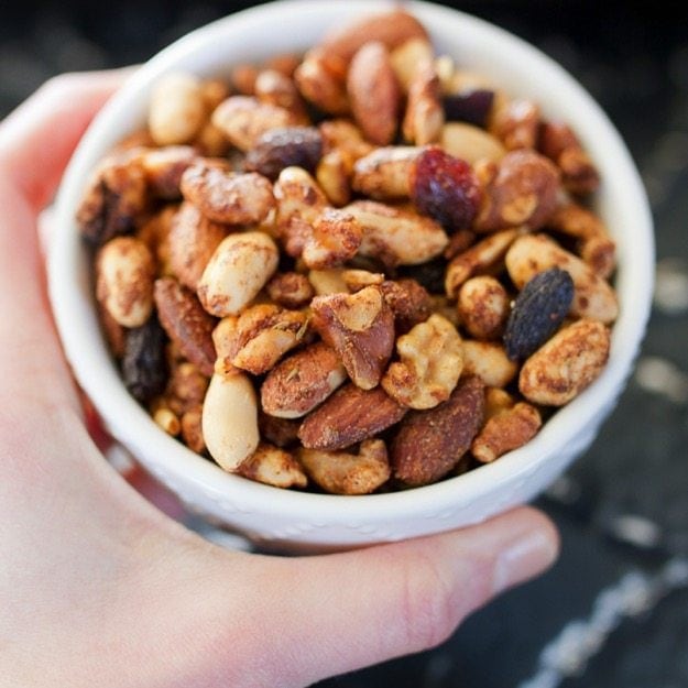 PIN THIS --> Cajun Trail Mix A woman\'s hand holding a small white bowl filled with cajun trail mix.
