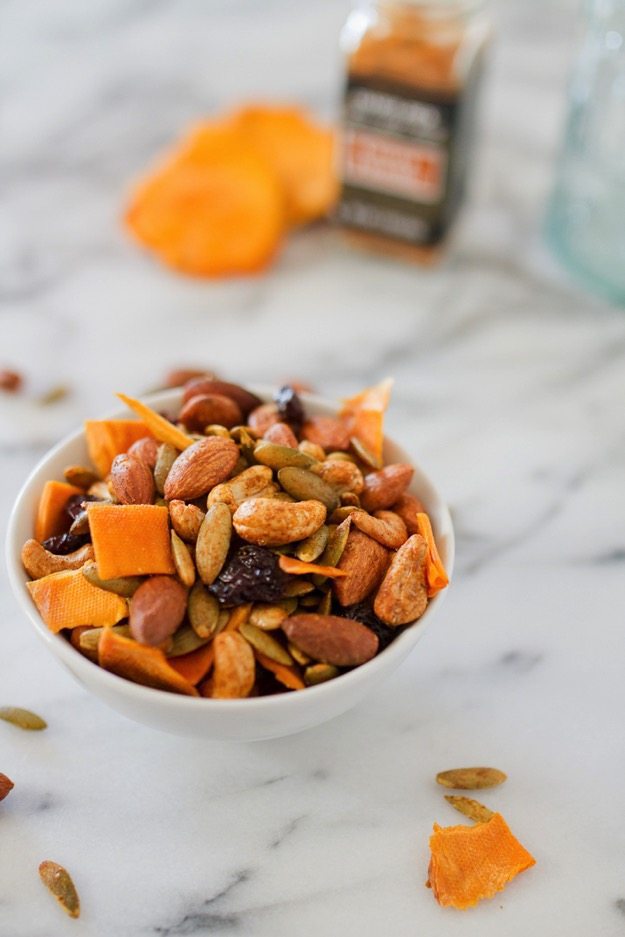 SAVE THIS FOR LATER --> Mango Curry Trail Mix Mango curry trail mix in a white bowl on a marble counter with curry powder in the background.