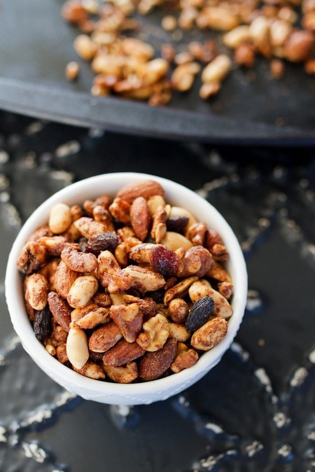 PIN THIS --> Spicy Cajun Trail Mix A woman\'s hand holding a small white bowl filled with cajun trail mix.