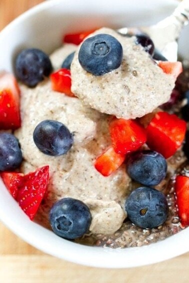 Cashew chia pudding served in a white bowl topped with fresh strawberries and blueberries.