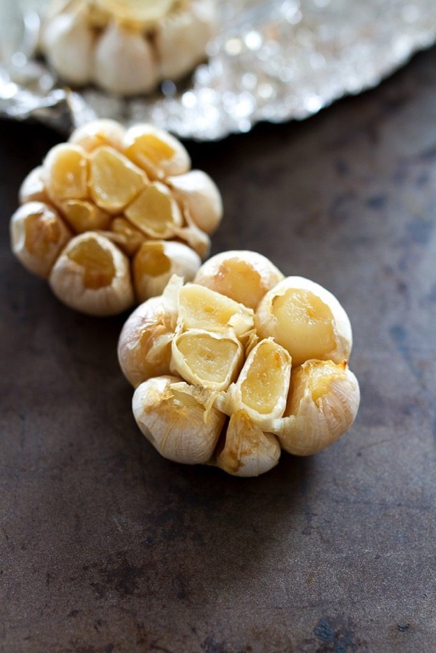 Pin this image to save the simple recipe for How to Make Roasted Garlic! Two heads of garlic on a baking sheet.