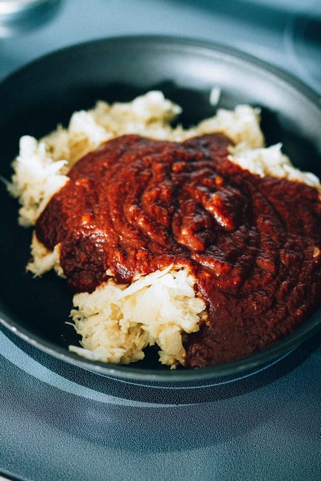 A vegan BBQ sandwich made with shredded hearts of palm, homemade BBQ sauce and a crunchy apple cider vinegar coleslaw. BBQ sauce spread on top of shredded hearts of palm in a bowl.