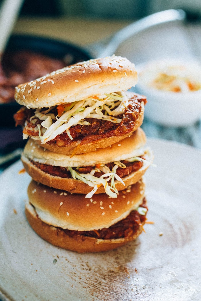 Vegan BBQ sandwiches made with shredded hearts of palm, homemade BBQ sauce and a crunchy apple cider vinegar coleslaw. Three hearts of palm BBQ sandwiches stacked on top of each other.