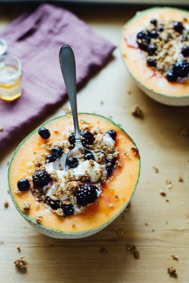 Cantaloupe Breakfast Bowls served with a spoon filled with Greek Yogurt, fresh blackberries, granola and honey.