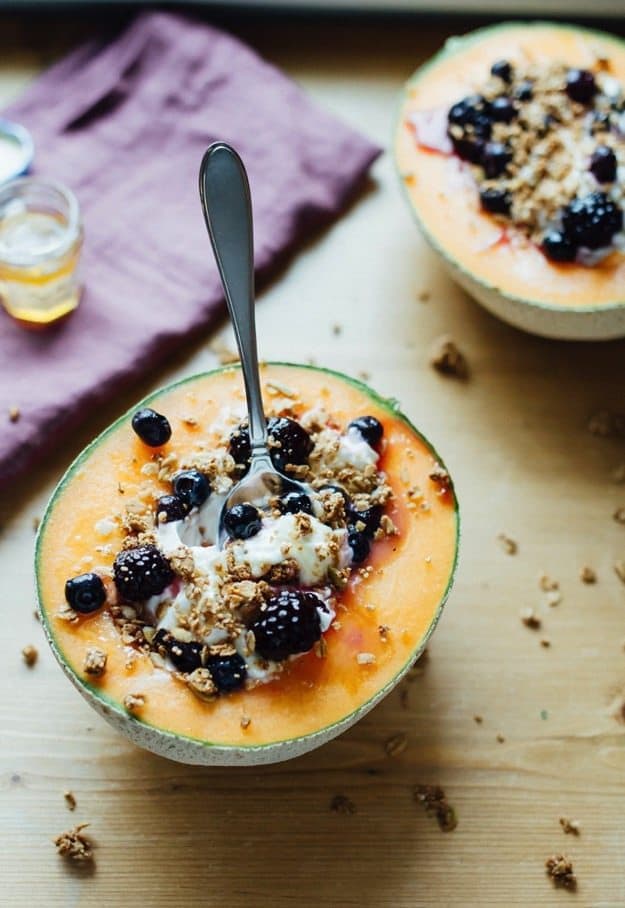 Pin this image to save these Cantaloupe Breakfast Bowls with Greek Yogurt, Berries, Granola and Honey! Cantaloupe Breakfast Bowls served with a spoon filled with Greek Yogurt, fresh blackberries, granola and honey.