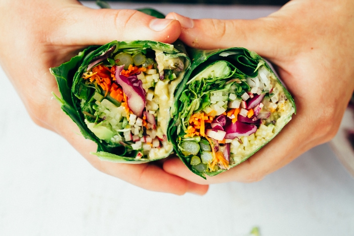 Save the recipe for these delicious hummus collard wraps! Two hands holding two halves of hummus collard wraps packed with chopped veggies.