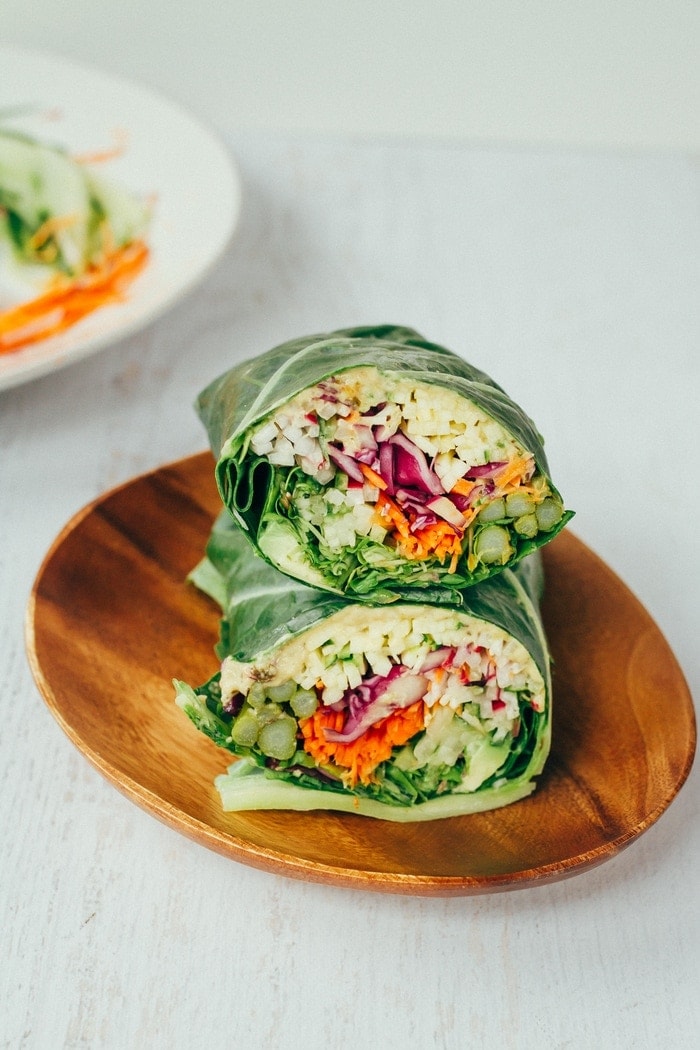 EASY and HEALTHY veggie packed hummus collard wraps! Collard green wraps filled with hummus and chopped veggies sitting on a wood plate.