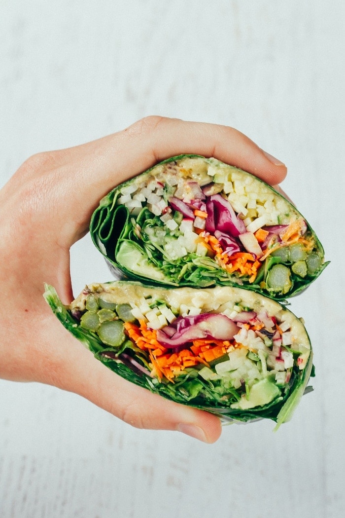 Save the recipe for these EASY and HEALTHY veggie packed hummus collard wraps! Hand holding two halves of veggie packed hummus collard wraps.