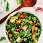 Mustard Greens salad with roasted potatoes and tomatoes served in a white bowl next to a wooden spoon.