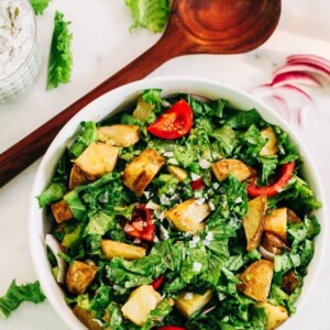 Mustard Greens salad with roasted potatoes and tomatoes served in a white bowl next to a wooden spoon.