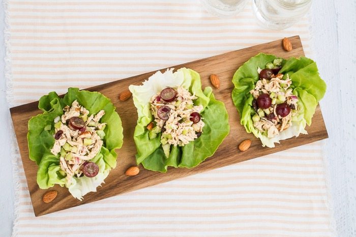 Almond Butter Chicken Salad -- perfect for serving in lettuce wraps or on your favorite sandwich bread. Three lettuce wraps filled with almond butter chicken salad served on a wooden cutting board.
