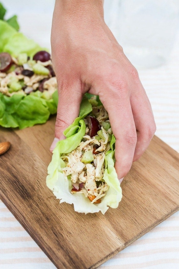 Almond Butter Chicken Salad -- perfect for serving in lettuce wraps or on your favorite sandwich bread. Almond butter chicken salad made with almonds, celery and grapes in lettuce cups. Hand picking up a lettuce cup.