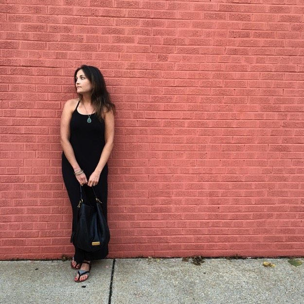 Pin this image to save my experience with hypothalamic amenorrhea! Girl dressed in all black standing against a red brick wall.