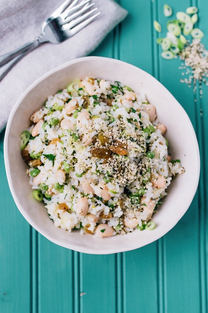 This Mediterranean-inspired rice salad with creamy cannellini beans and Hemp Hearts can be served warm or chilled and makes a lovely vegetarian main or a flavorful side. Lemony rice salad served in a white bowl with white beans, green beans, hemp hearts and golden raisins.