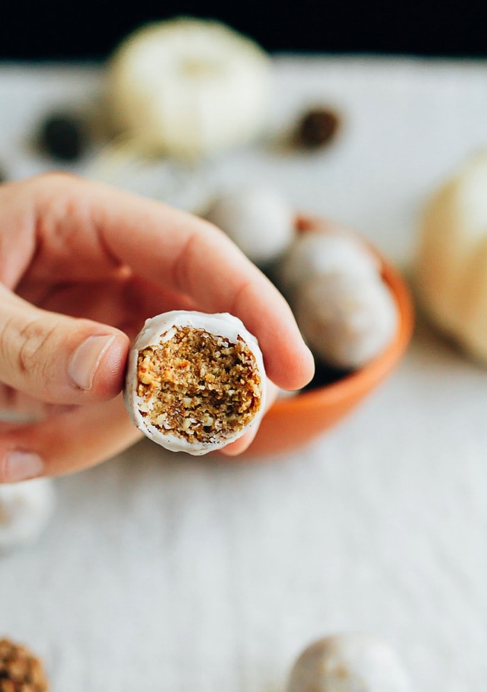 These No Bake Pumpkin Spice Donut Holes are packed full of pumpkin spice flavor and covered in a coconut maple glaze. Vegan, gluten-free and absolutely delicious. Hand holding a pumpkin spice donut hole with a bite taken out of it.