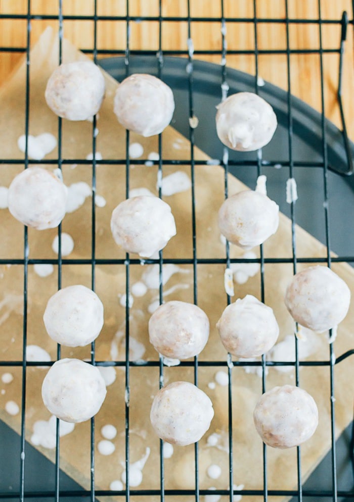 No Bake Pumpkin Spice Donut Holes // Vegan, Gluten-Free, Paleo Pumpkin size donut holes on a rack over parchment paper, being glazed with the coconut frosting.