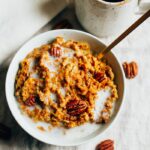 Slow cooker pumpkin pie oatmeal served in a white bowl topped with pecans and a splash of milk.