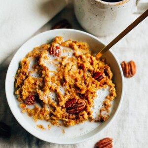 Slow cooker pumpkin pie oatmeal served in a white bowl topped with pecans and a splash of milk.