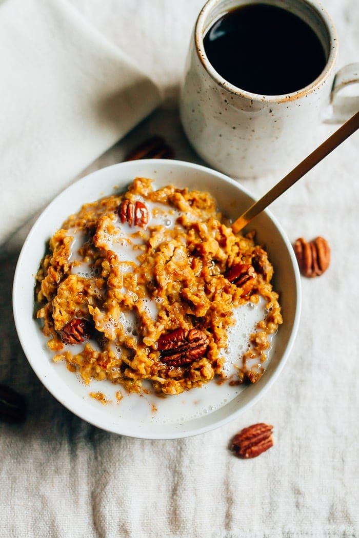 Pin this image to save this healthy Slow Cooker Pumpkin Pie Oatmeal recipe! Slow cooker pumpkin pie oatmeal served in a white bowl topped with pecans and a splash of milk.