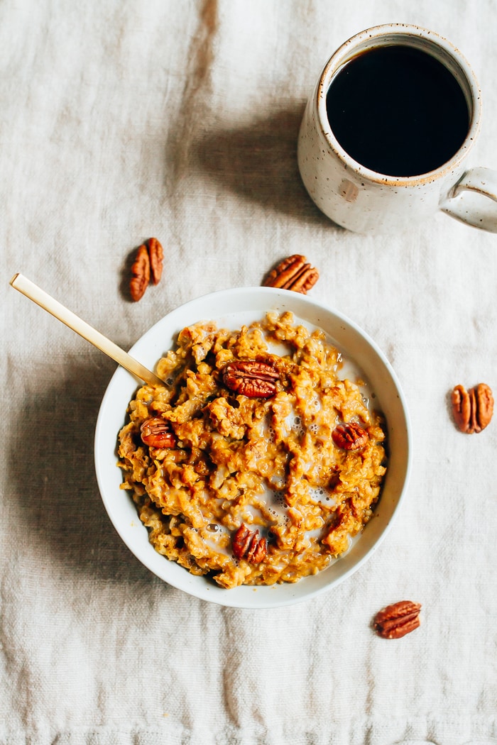 Make this HEALTHY Slow Cooker Pumpkin Pie Oatmeal recipe! Overhead photo of Slow Cooker Pumpkin Pie Oatmeal in a white bowl with pecans scattered around the bowl.