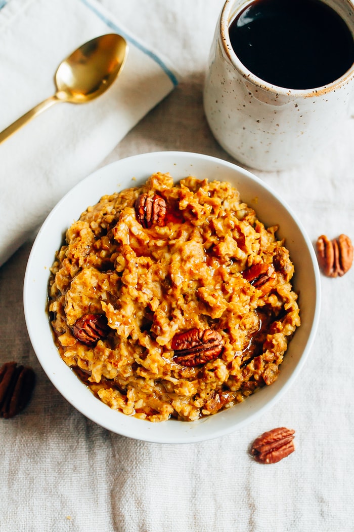 Save this recipe for healthy Slow Cooker Pumpkin Pie Oatmeal! Overhead photo of Slow Cooker Pumpkin Pie Oatmeal in a white bowl. Mug of coffee in the background.