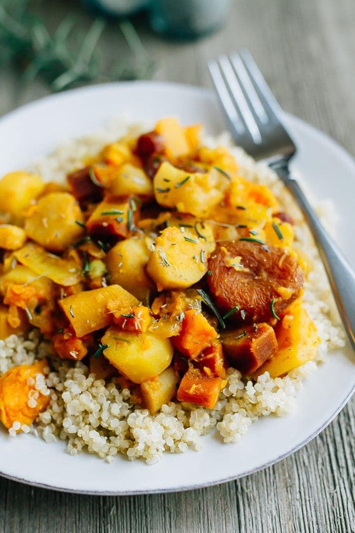 A slow simmered root vegetable tagine with apricots and rosemary! Serve this vegetarian dish as a side or over rice or quinoa for a complete meal. Root vegetable tagine with rosemary and apricots served over a plate of brown rice.