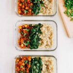 Three curried chickpea bowls served in glass tupperware containers alongside brown rice and spinach.