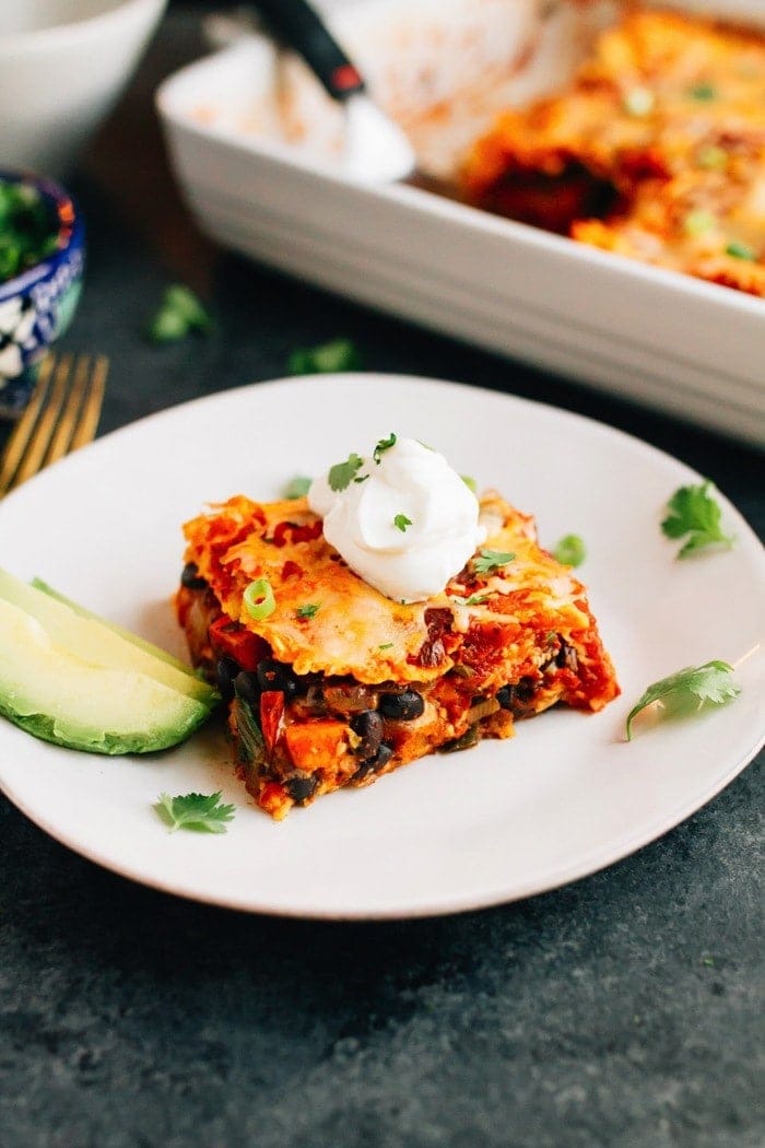 A healthy make-ahead dish the whole family will love, this sweet potato black bean enchilada bake is layered with tortillas, sweet potatoes, black beans, cheese and a homemade enchilada sauce. Vegetarian, gluten-free and absolutely delicious! Slice of sweet potato black bean enchilada bake layered with tortillas, sweet potatoes, black beans, cheese and a homemade enchilada sauce with slices of avocado on the side. Remaining enchilada bake in baking dish behind.