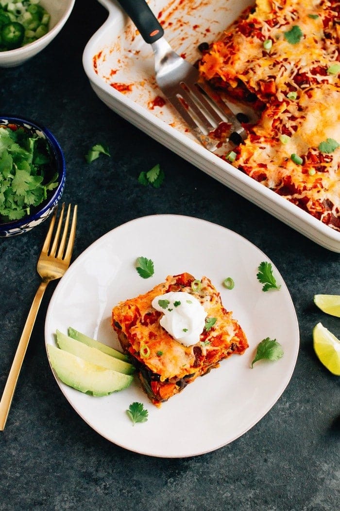 A healthy make-ahead dish the whole family will love, this sweet potato black bean enchilada bake is layered with tortillas, sweet potatoes, black beans, cheese and a homemade enchilada sauce. Vegetarian, gluten-free and absolutely delicious! Slice of sweet potato black bean enchilada bake layered with tortillas, sweet potatoes, black beans, cheese and a homemade enchilada sauce with slices of avocado on the side. Remaining enchilada bake in baking dish behind.
