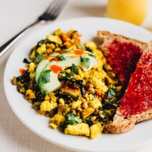 Tofu scramble topped with avocado slices served alongside bread topped with jam.