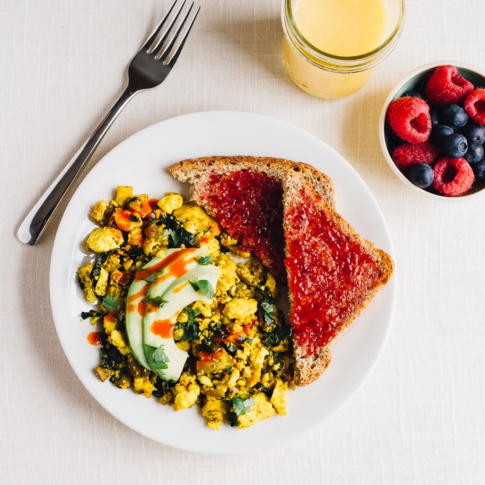 PIN THIS --> Golden Tofu Scramble Tofu breakfast scrambled topped with avocado slices and served with two pieces of toast topped with jam.