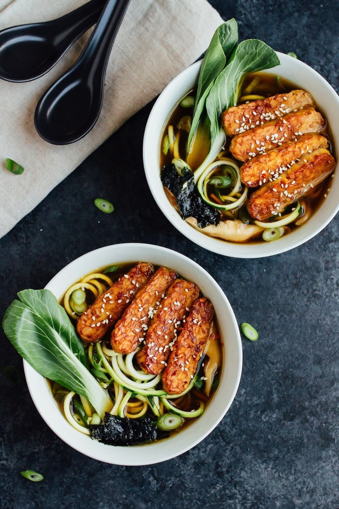 Overhead photo of vegan zucchini noodle ramen bowls served in white bowls on dark grey countertop.