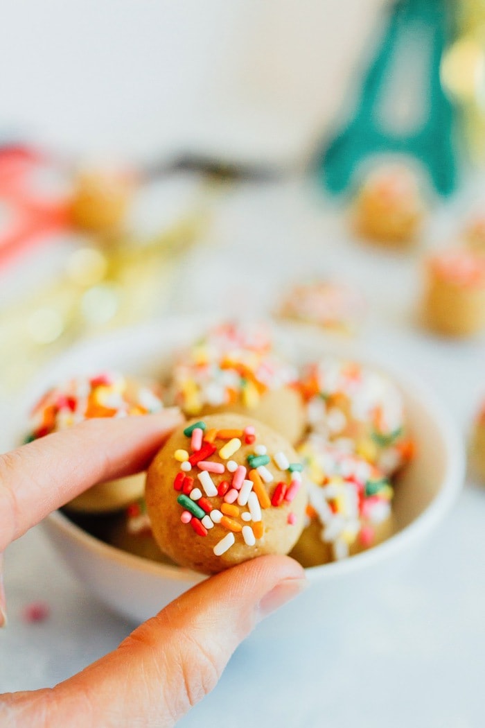 Have your cake and eat it too! These Vanilla Bake balls are moist, fluffy and taste like cake, but they're made with healthy ingredients like chickpeas, vegan protein powder and cashew butter. Vegan + gluten-free. A woman\'s hand holding a cake ball topped with rainbow sprinkles.