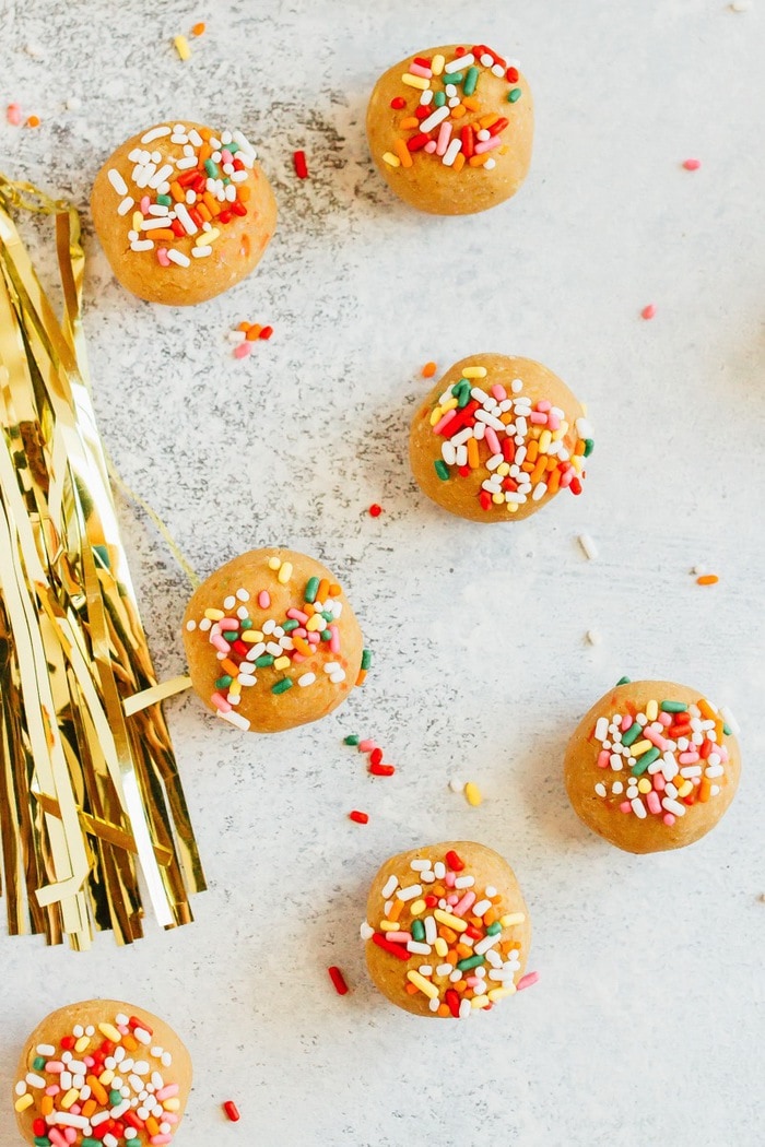 Have your cake and eat it too! These Vanilla Bake balls are moist, fluffy and taste like cake, but they're made with healthy ingredients like chickpeas, vegan protein powder and cashew butter. Vegan + gluten-free. Vanilla cake balls spread out on a counter topped with rainbow sprinkles.