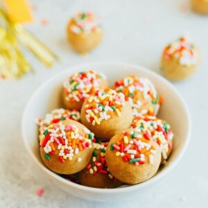 Vanilla cake balls topped with rainbow sprinkles in a white bowl.