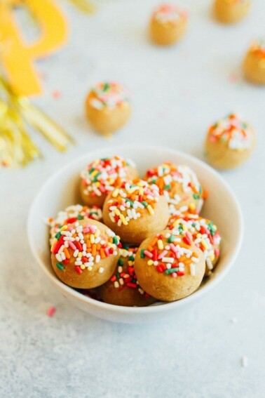 Vanilla cake balls topped with rainbow sprinkles in a white bowl.